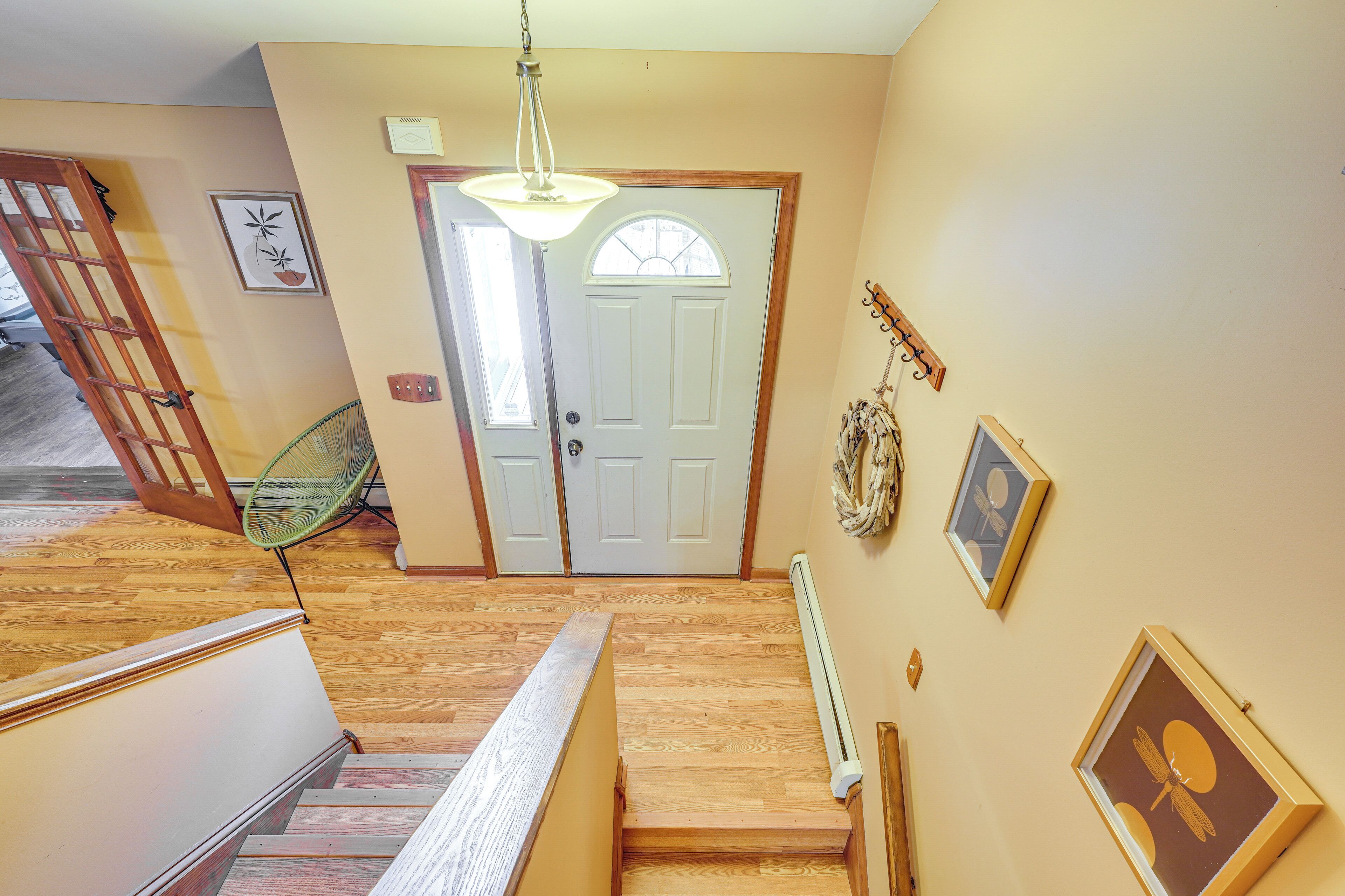 A staircase leading to a door with a white frame, a hanging light fixture, and framed artwork on the walls.
