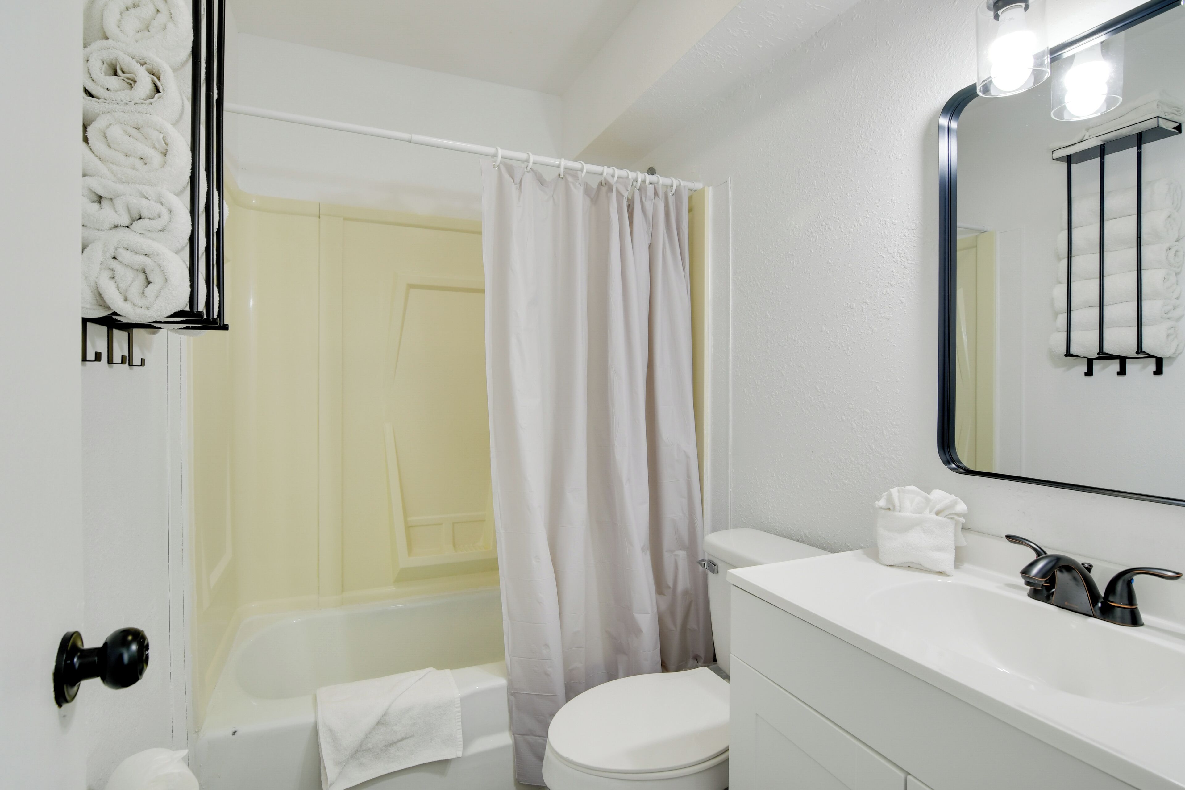 A bathroom with a white bathtub, a toilet, and a sink with a mirror above it.