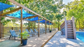 Une terrasse en bois avec des auvents bleus, des chaises longues, une piscine et un toboggan.