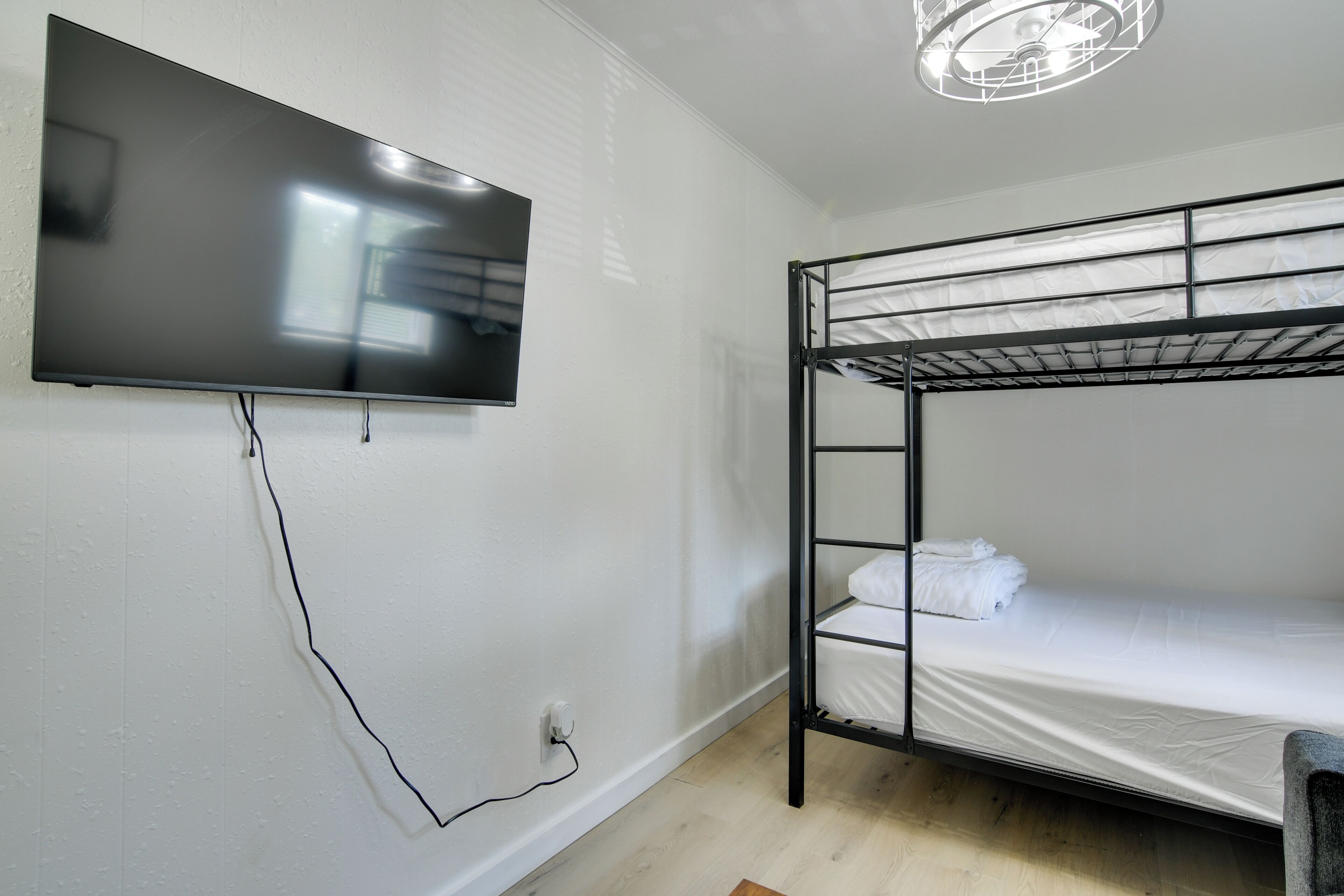A bunk bed with a TV mounted on the wall, a power outlet, and a ceiling light fixture.