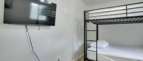 A bunk bed with a TV mounted on the wall, a power outlet, and a ceiling light fixture.