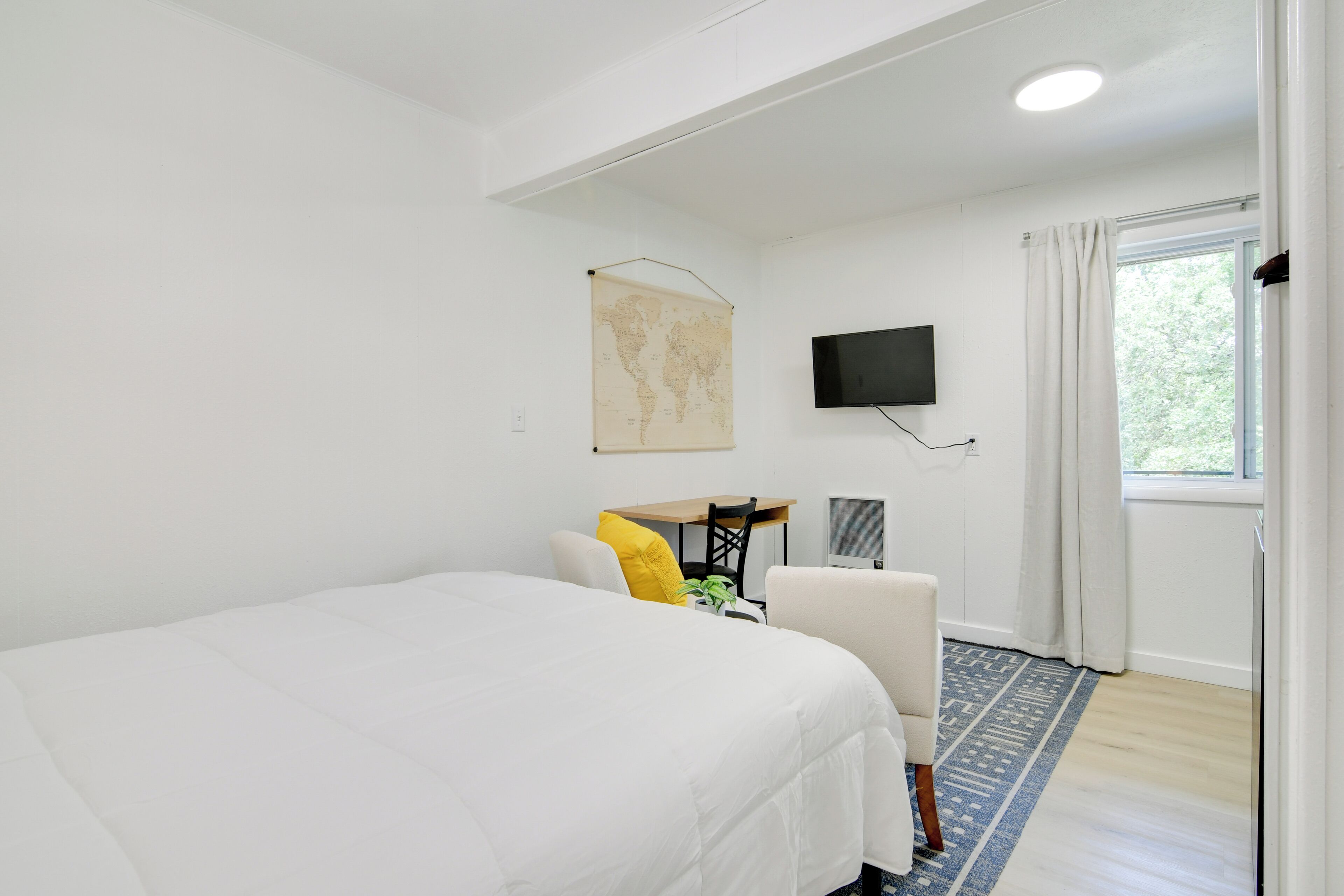 Una habitación de hotel con una cama grande, un escritorio, una silla, un televisor de pantalla plana y una ventana con cortinas.