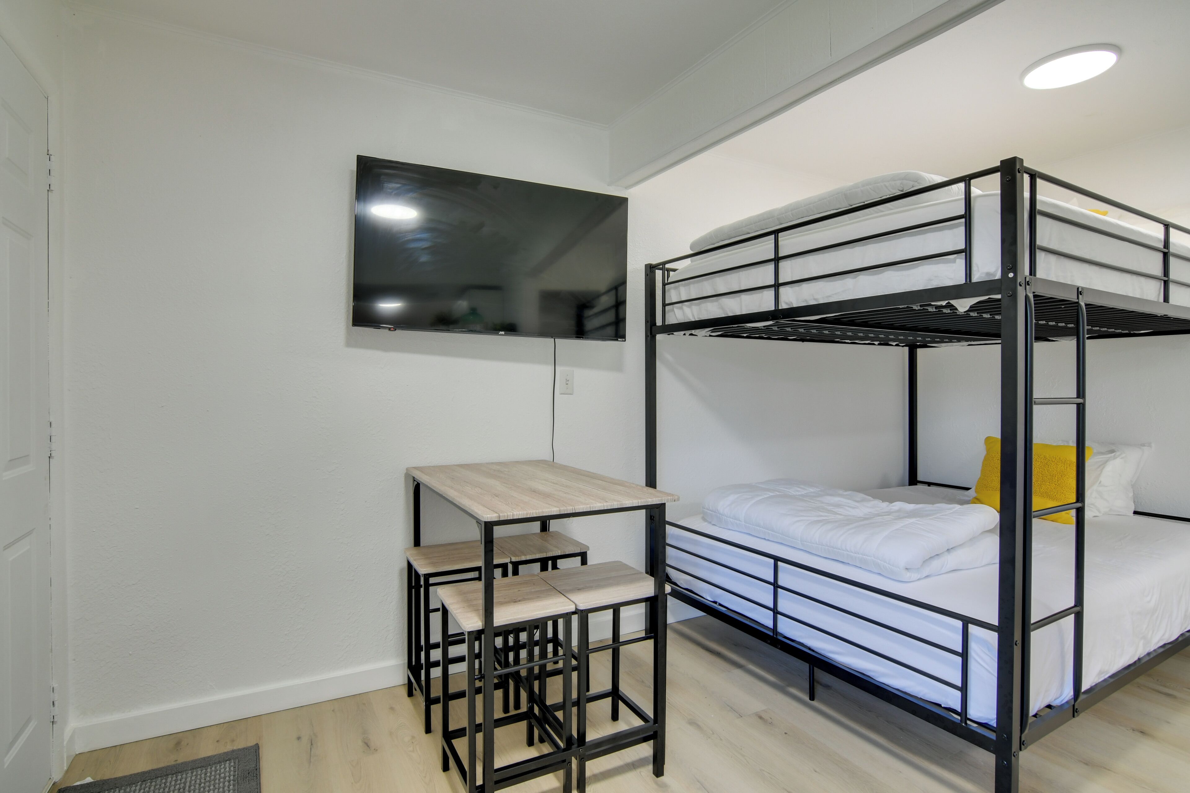 Ein Stockbett mit Schreibtisch und Stuhl, ein kleines Fenster und eine weiße Wand.