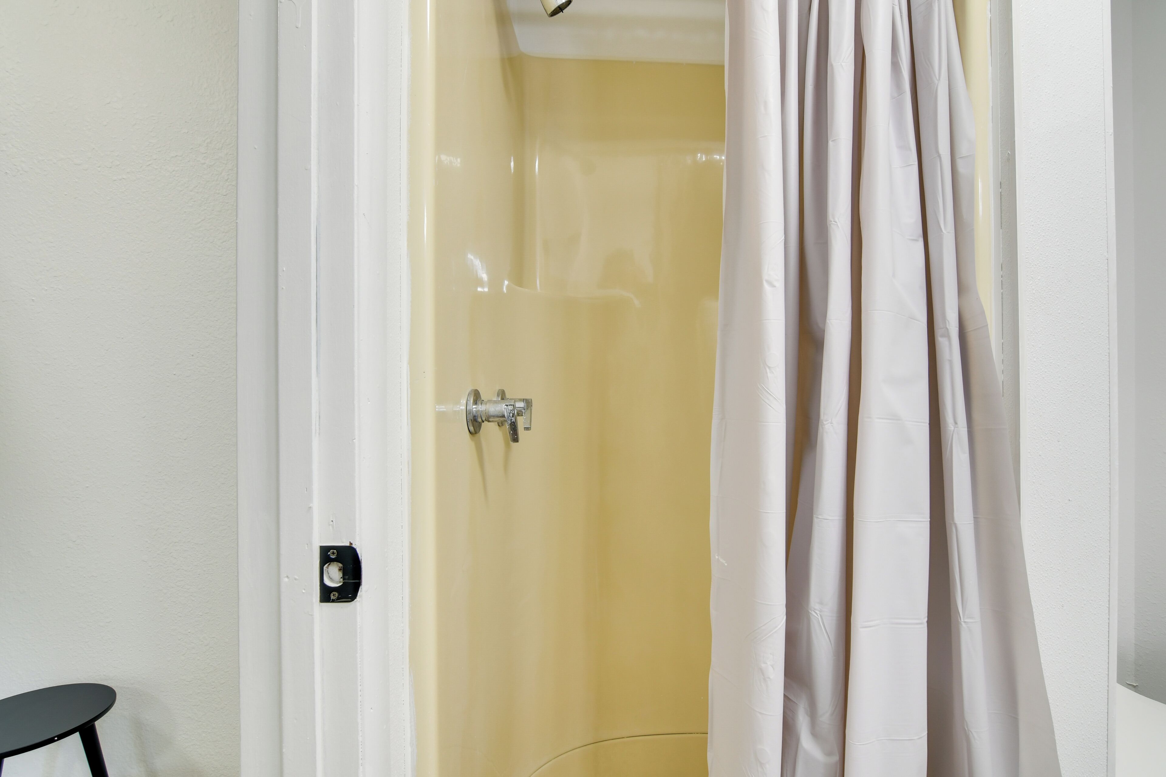 Un baño con una pared amarilla, una cortina de ducha blanca y una silla negra.