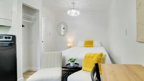 Une chambre d’hôtel de taille réduite, comprenant un lit, une petite table, une chaise, une plante en pot et un lave-linge.