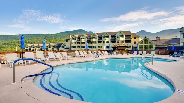 A resort pool with lounge chairs and umbrellas, surrounded by a building with multiple balconies and a mountain backdrop. - 1 Mi to Loon Mountain: Lincoln Haven w/ Balcony (Lincoln)