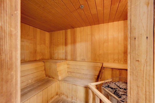 Eine Holzsauna mit Bänken und einem Metallkorb.