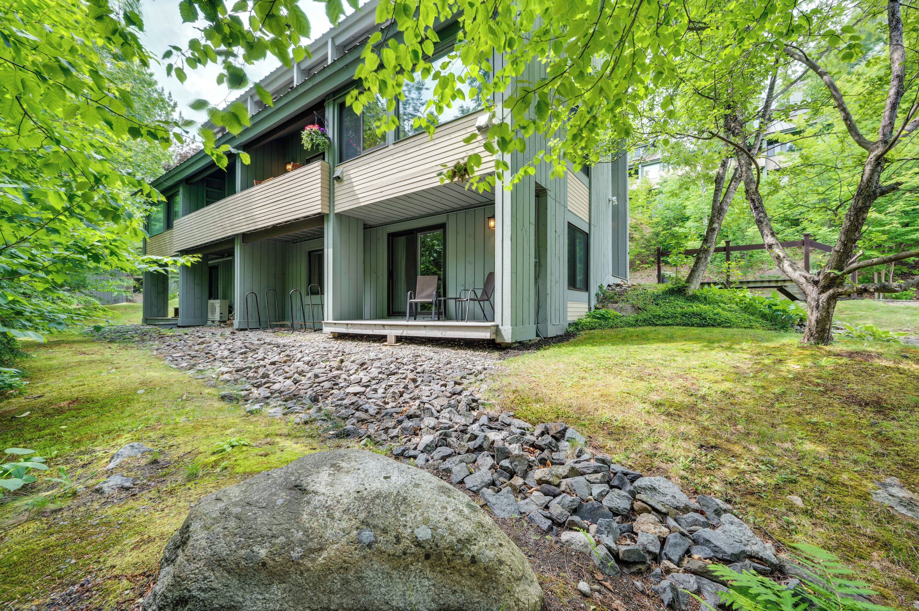 Una moderna casa a due piani con portico coperto, immersa in un paesaggio naturale ricco di rocce e vegetazione.