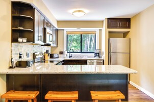 Una cocina moderna con una isla grande, armarios oscuros y vistas al exterior.