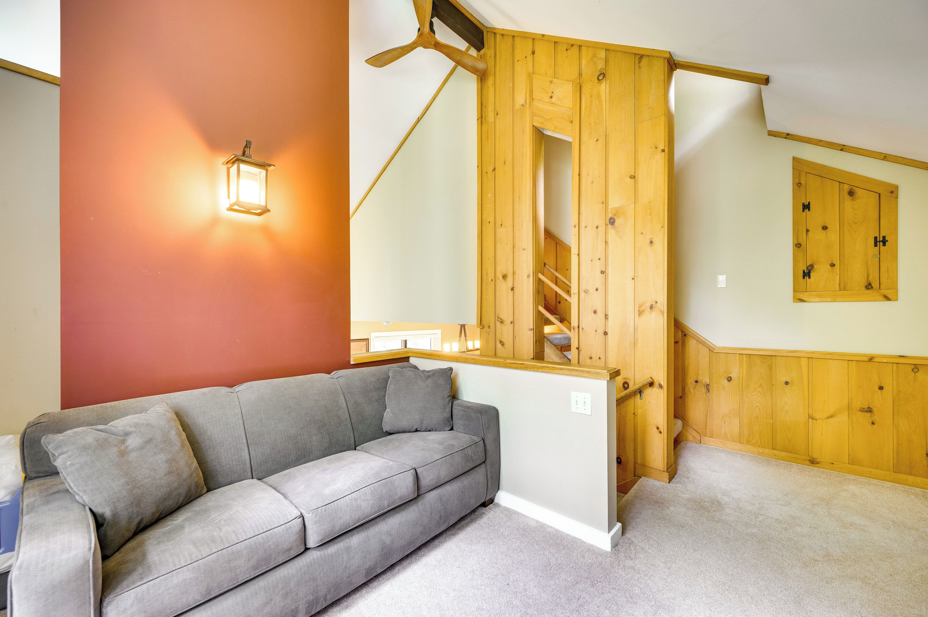 Una habitación con un sofá gris, una escalera de madera y una lámpara fijada a la pared.