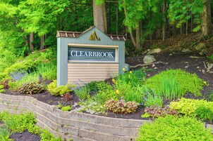 A sign for 'CLEARBROOK' surrounded by a landscaped garden with various plants and a stone retaining wall.