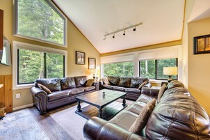 Amplia sala de estar con sofás de cuero, una mesa de centro y ventanas grandes con vistas al exterior.