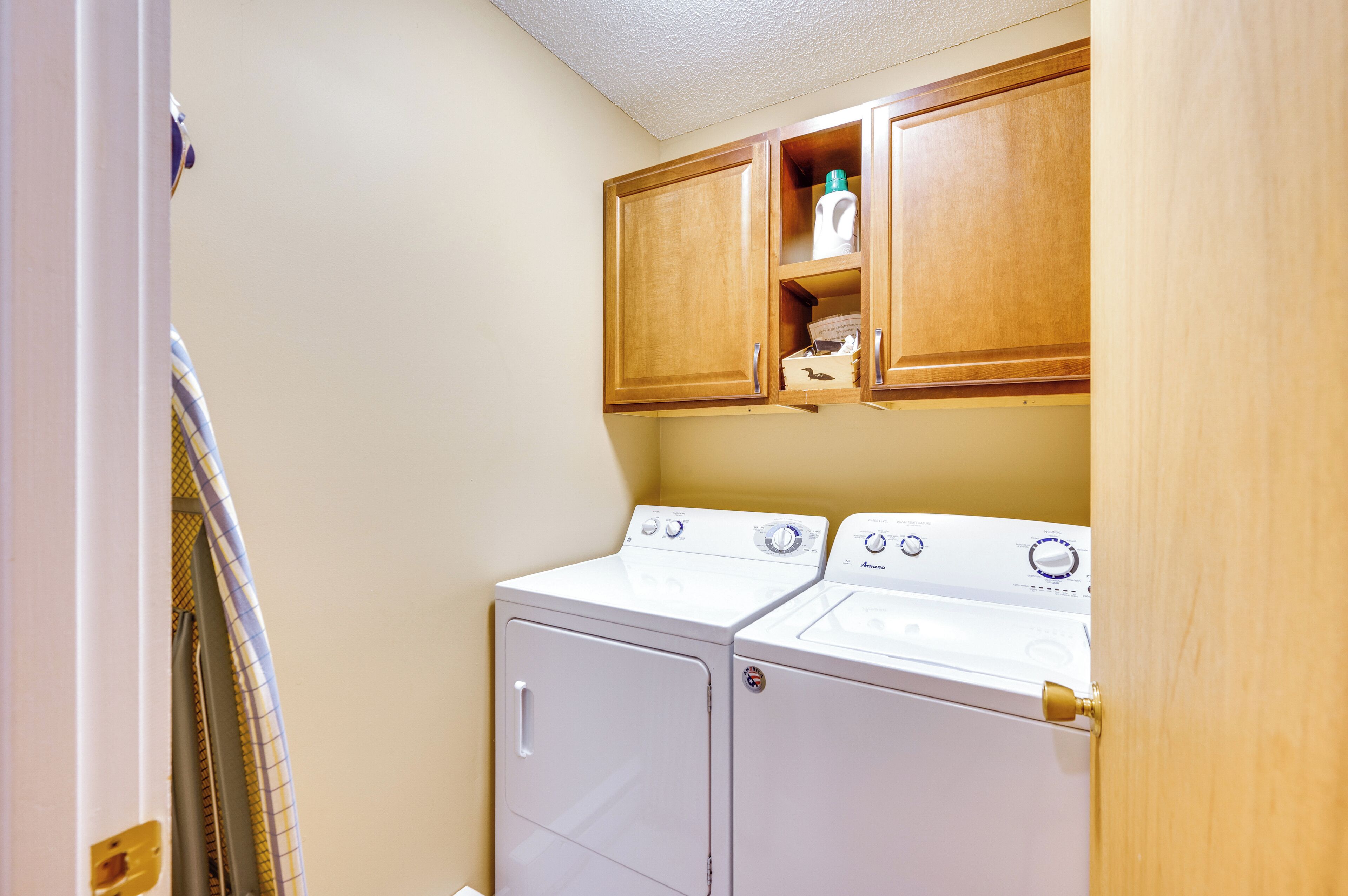 A laundry room with two white front-loading washers and dryers, wooden cabinets above, and a towel rack to the left.