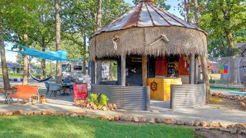 A rustic gazebo with a thatched roof, surrounded by trees and a small seating area with benches.