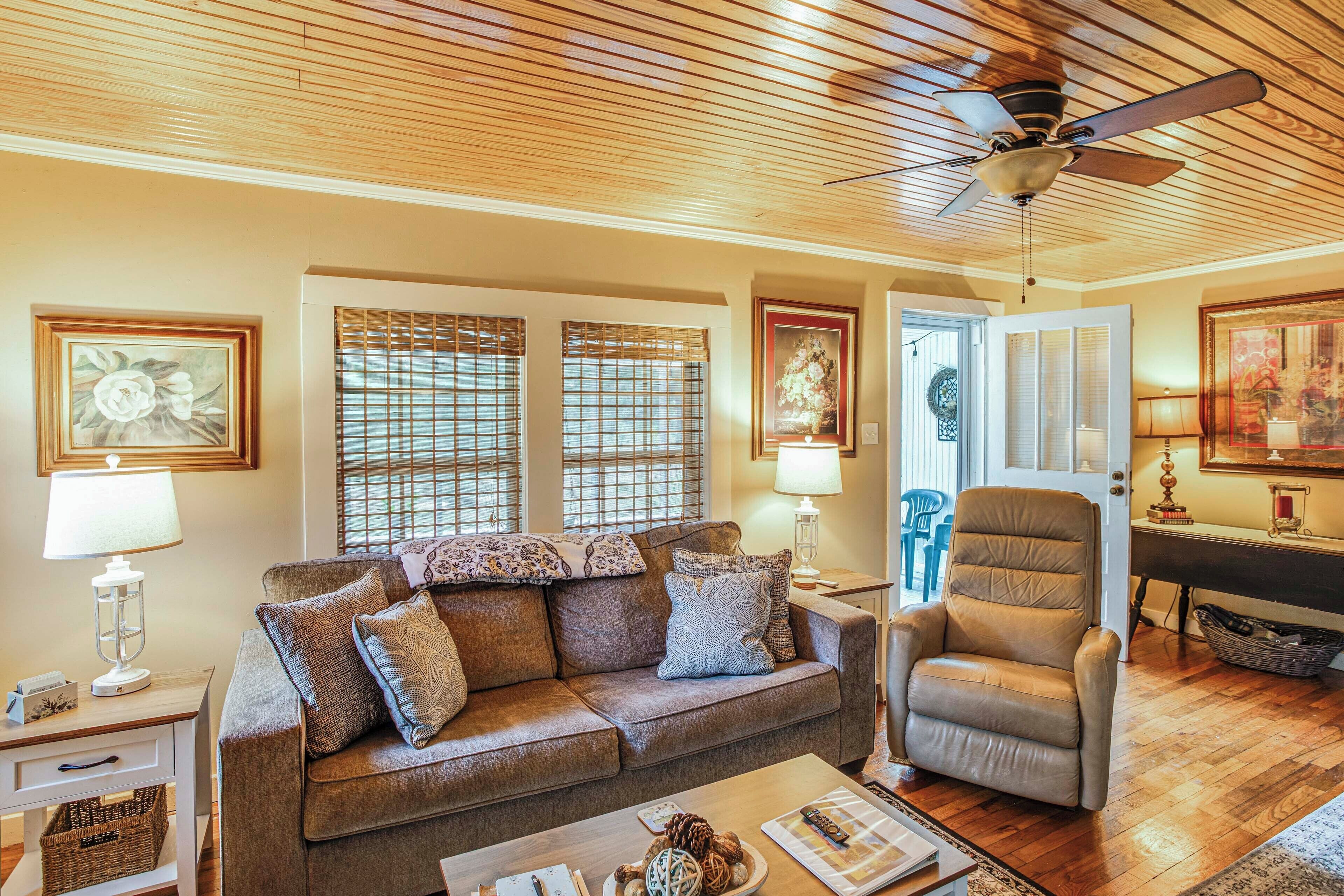 Un salon avec un canapé marron, un fauteuil beige, un plafond en bois et un ventilateur de plafond.