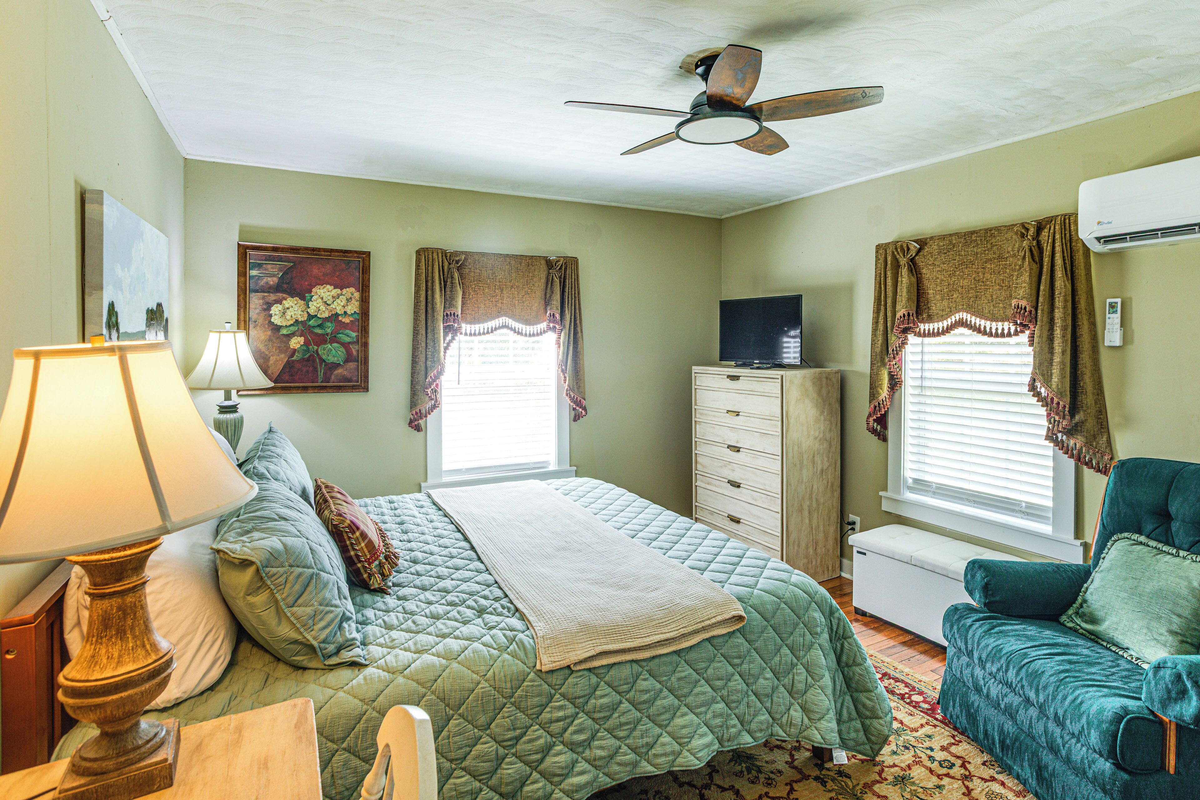 Ein Schlafzimmer mit Bett, Kommode, Fernseher und Deckenventilator.