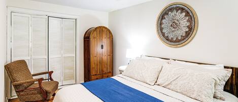 A bedroom with a bed, a wooden chair, a wardrobe, and a ceiling fan.