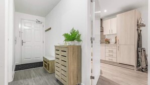 Un passadís amb un armari de fusta, una planta en test i una porta que dona a una cuina.