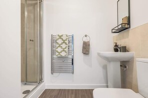 Ein Badezimmer mit Duschkabine aus Glas, einem Handtuchhalter mit gemusterten Handtüchern, einem Waschbecken und einer Toilette.