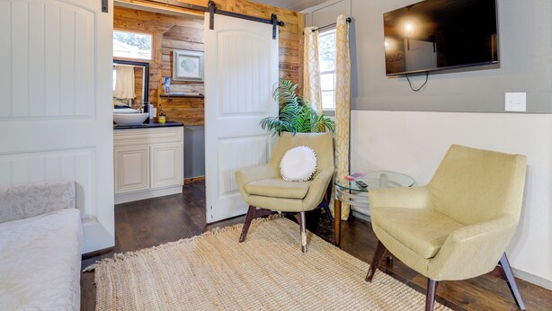 A room with a bed, a chair, a TV mounted on the wall, and a sliding door leading to a kitchen area. - Pet-friendly Grand Lake Studio w/ Outdoor Space (Grove)