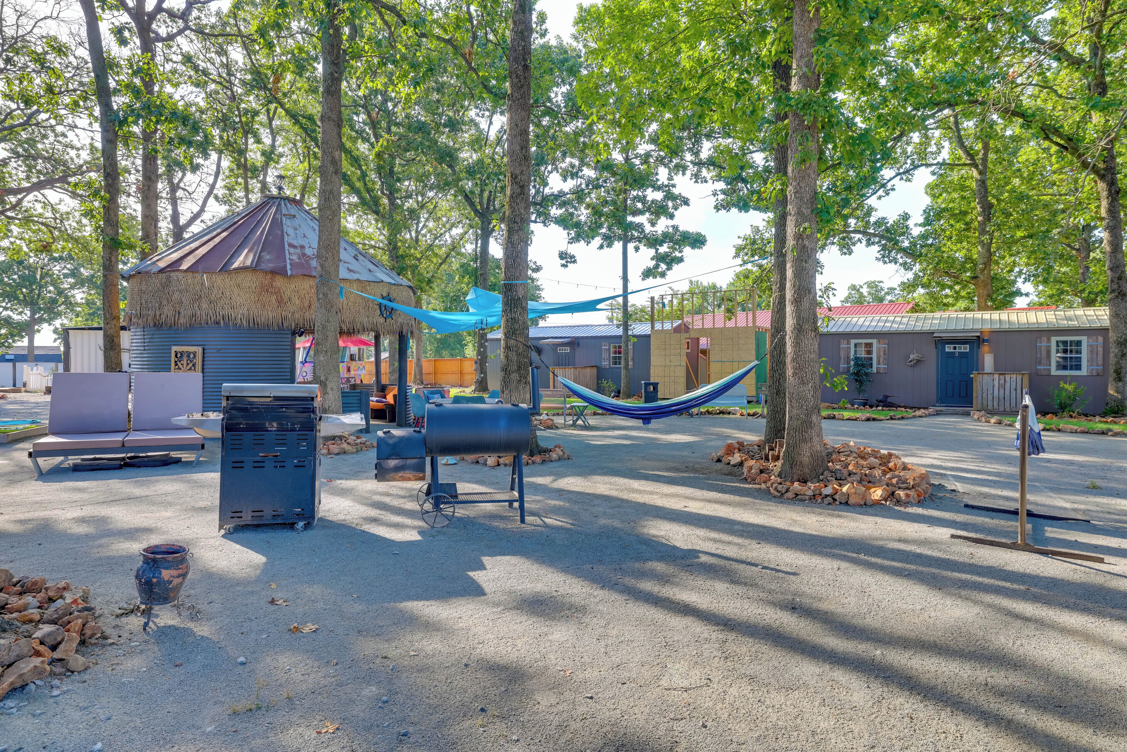 Un terrain de camping doté d’une structure à toit de chaume, d’un hamac et d’un barbecue.