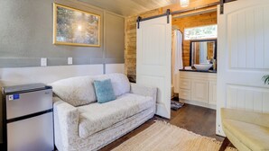 A cozy room with a sofa, a small refrigerator, a rug, and a sliding door leading to a bathroom with a sink and mirror. - Pet-friendly Grand Lake Studio w/ Outdoor Space (Grove)