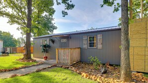 A single-story mobile home with a front porch, a small garden area with a tree and a potted plant, and a gravel pathway leading to the entrance. - Pet-friendly Grand Lake Studio w/ Outdoor Space (Grove)