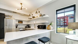 A modern kitchen with a large island, stainless steel appliances, and a view of a red building through the window.