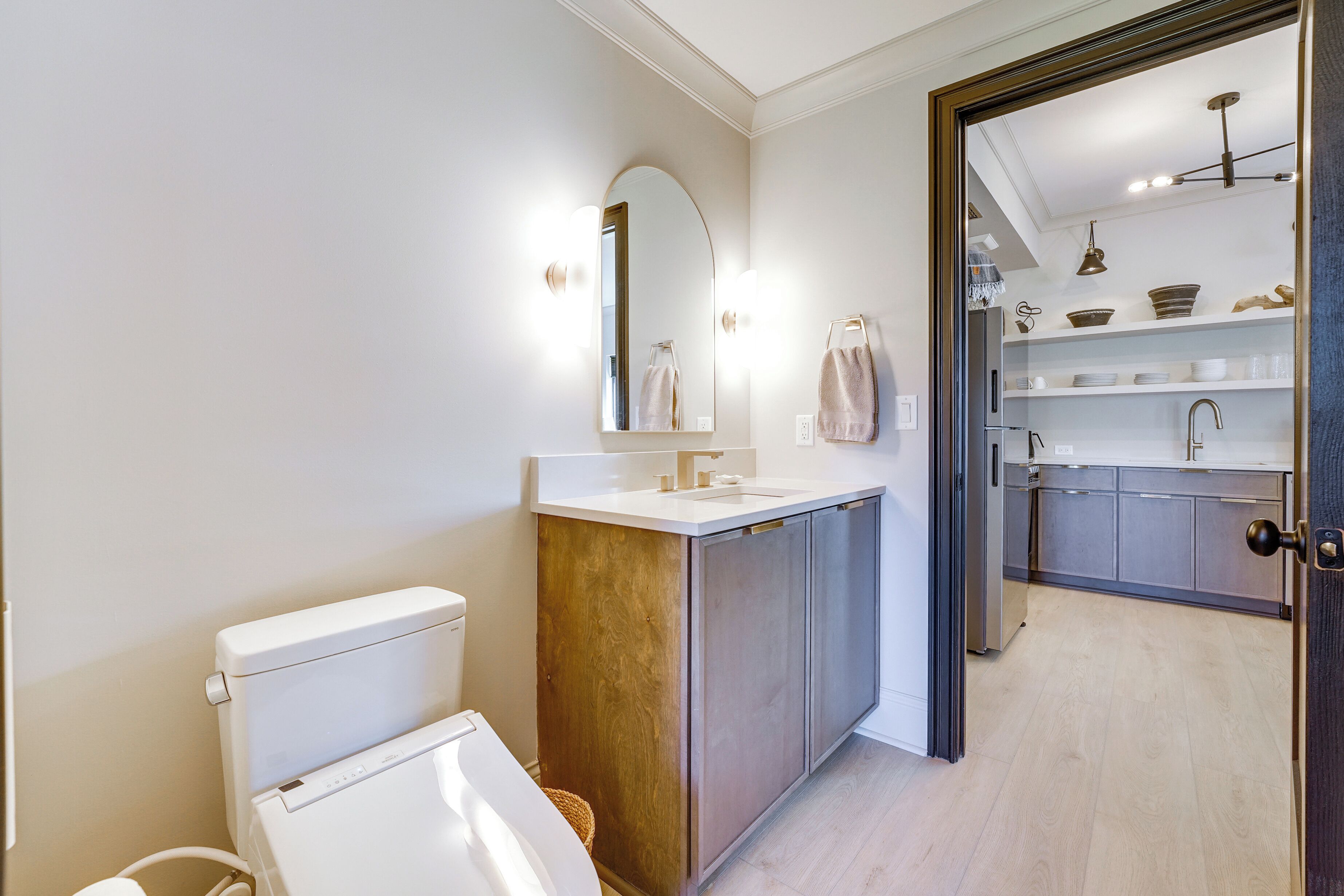 A modern bathroom with a toilet, sink, and mirror. There is a wooden cabinet and a shelf with towels.