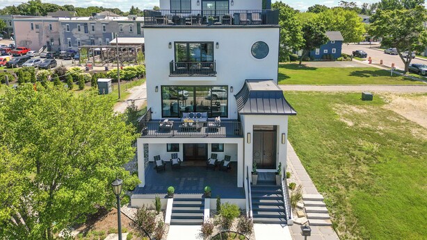 A modern multi-story building with a rooftop terrace, a covered outdoor seating area, and a well-maintained lawn.