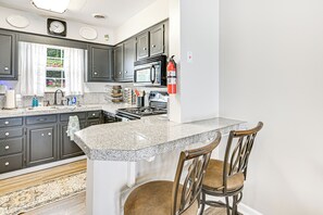 A kitchen with dark cabinets, a granite countertop, a microwave, a stove, and a fire extinguisher.