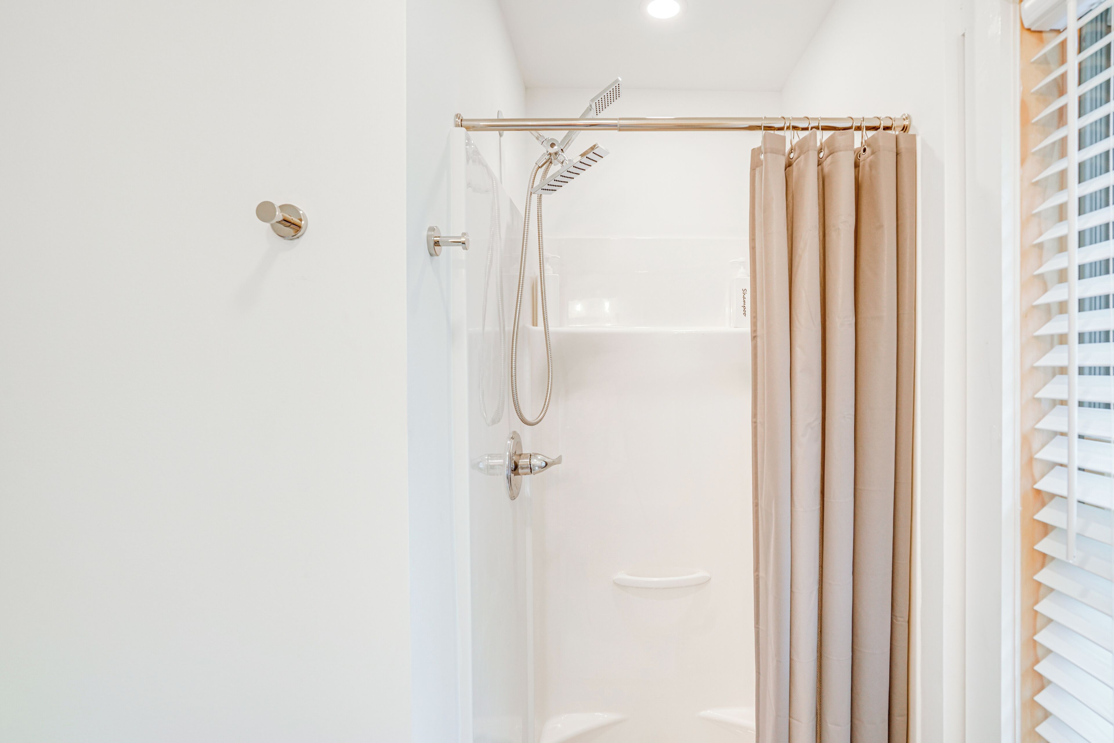 A modern bathroom with a glass-enclosed shower, beige curtains, and a white sink.