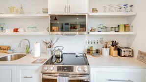 Una cocina moderna con armarios blancos, estufa de acero inoxidable y una isla con cubierta de vidrio.