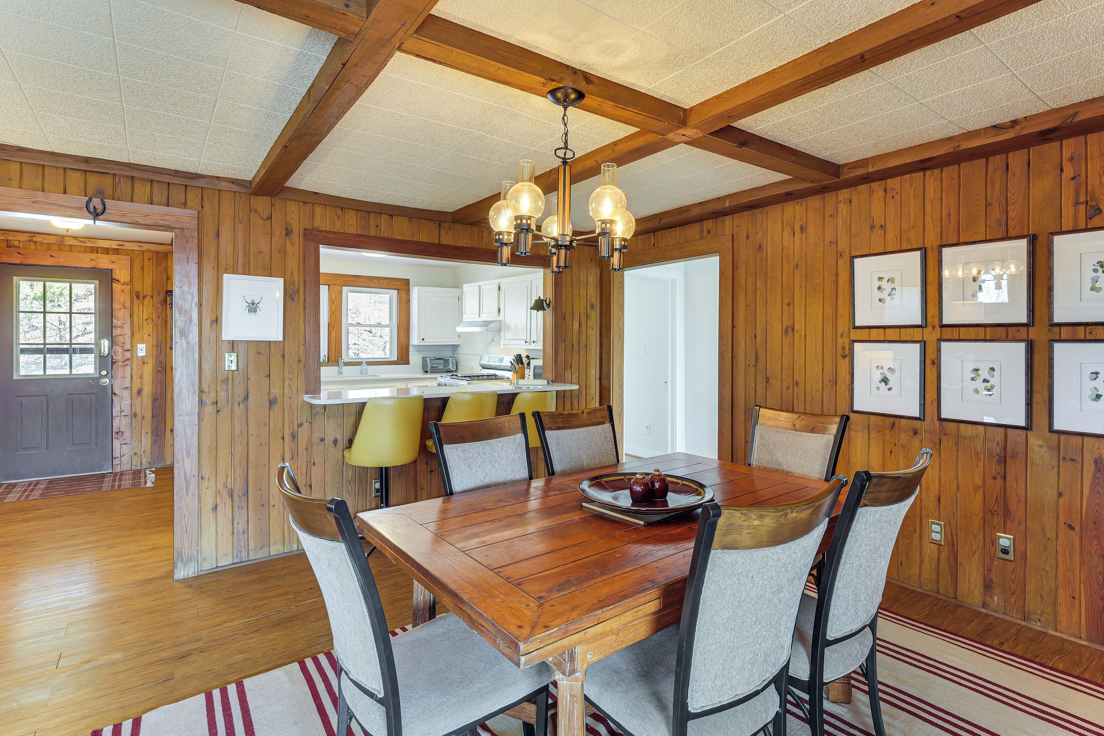 A wooden-paneled dining room with a large wooden table, six chairs, and a chandelier.