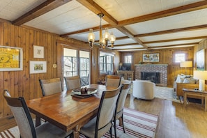 Une salle à manger en bois avec une cheminée en briques, des poutres apparentes en bois au plafond et une grande fenêtre.