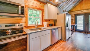 A modern kitchen with a stainless steel microwave, stove, and dishwasher, wooden cabinets, and a window providing natural light. - Kentucky Cabin Retreat w/ Covered Porch & Views (Lewisburg)