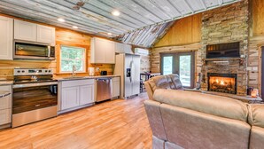 A modern kitchen with stainless steel appliances, a stone fireplace, and a wooden ceiling. - Kentucky Cabin Retreat w/ Covered Porch & Views (Lewisburg)