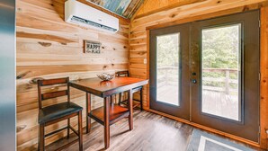 A wooden cabin interior with a dining table and chairs, a large window, and a door. - Kentucky Cabin Retreat w/ Covered Porch & Views (Lewisburg)