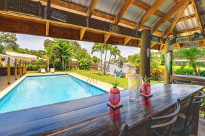 Un espace bar situé au bord de la piscine, avec une terrasse en bois, une piscine et une vue sur un paysage tropical.