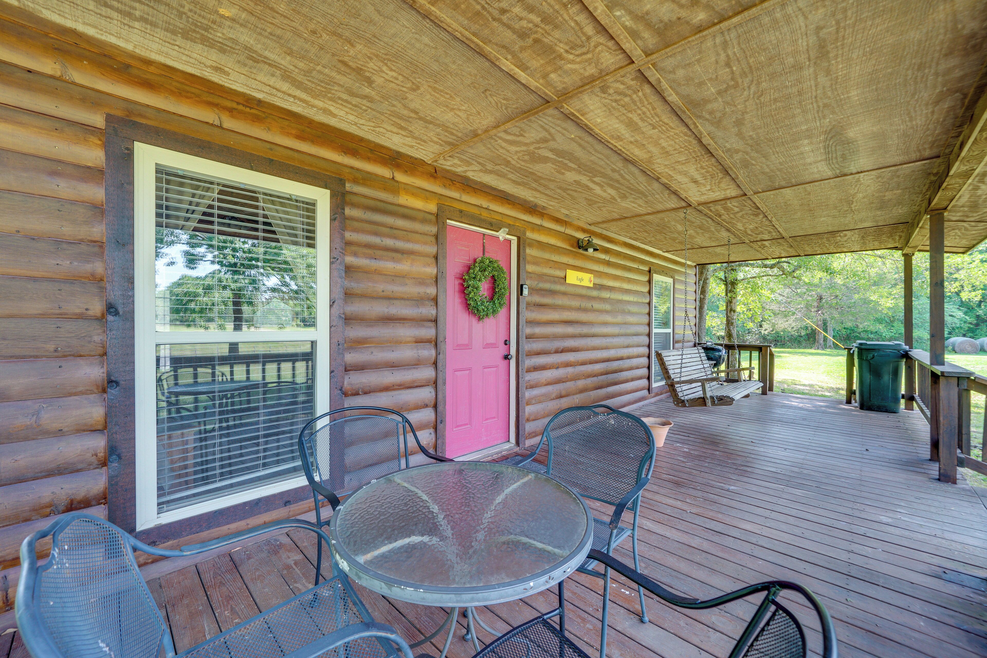 Une véranda avec une terrasse en bois, une porte rose et une table en verre avec des chaises.