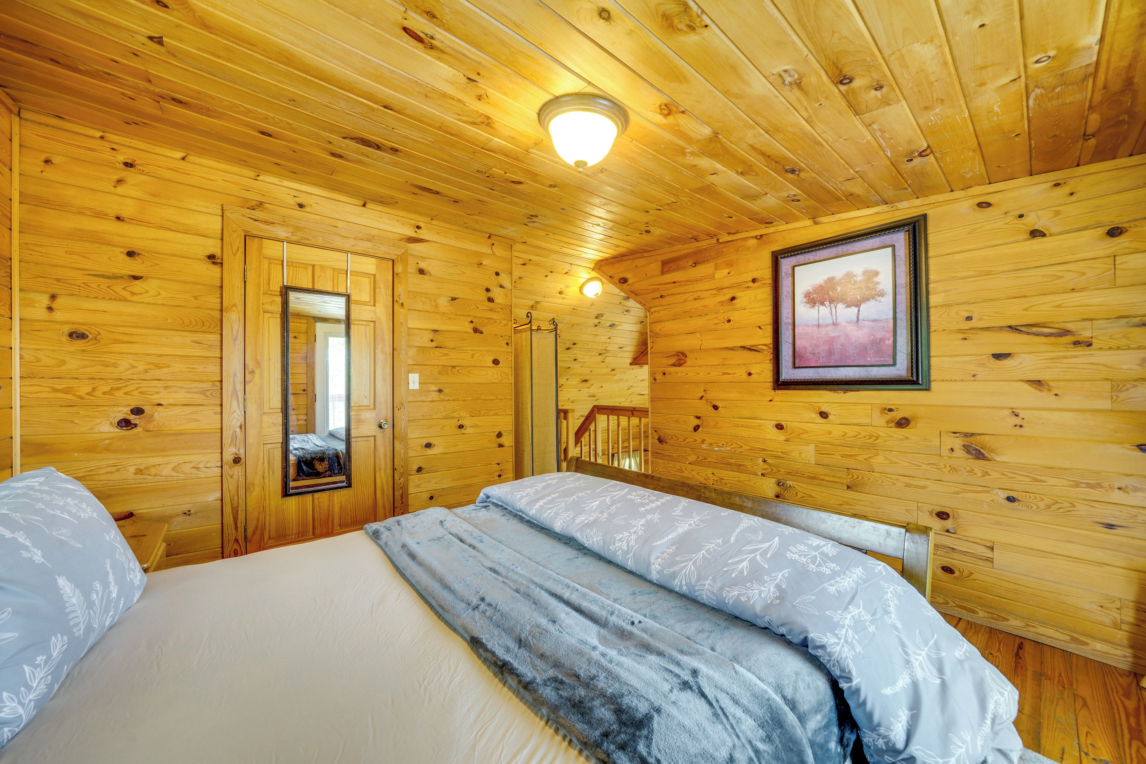 A wooden cabin bedroom with a bed, a mirror, and a framed picture on the wall.