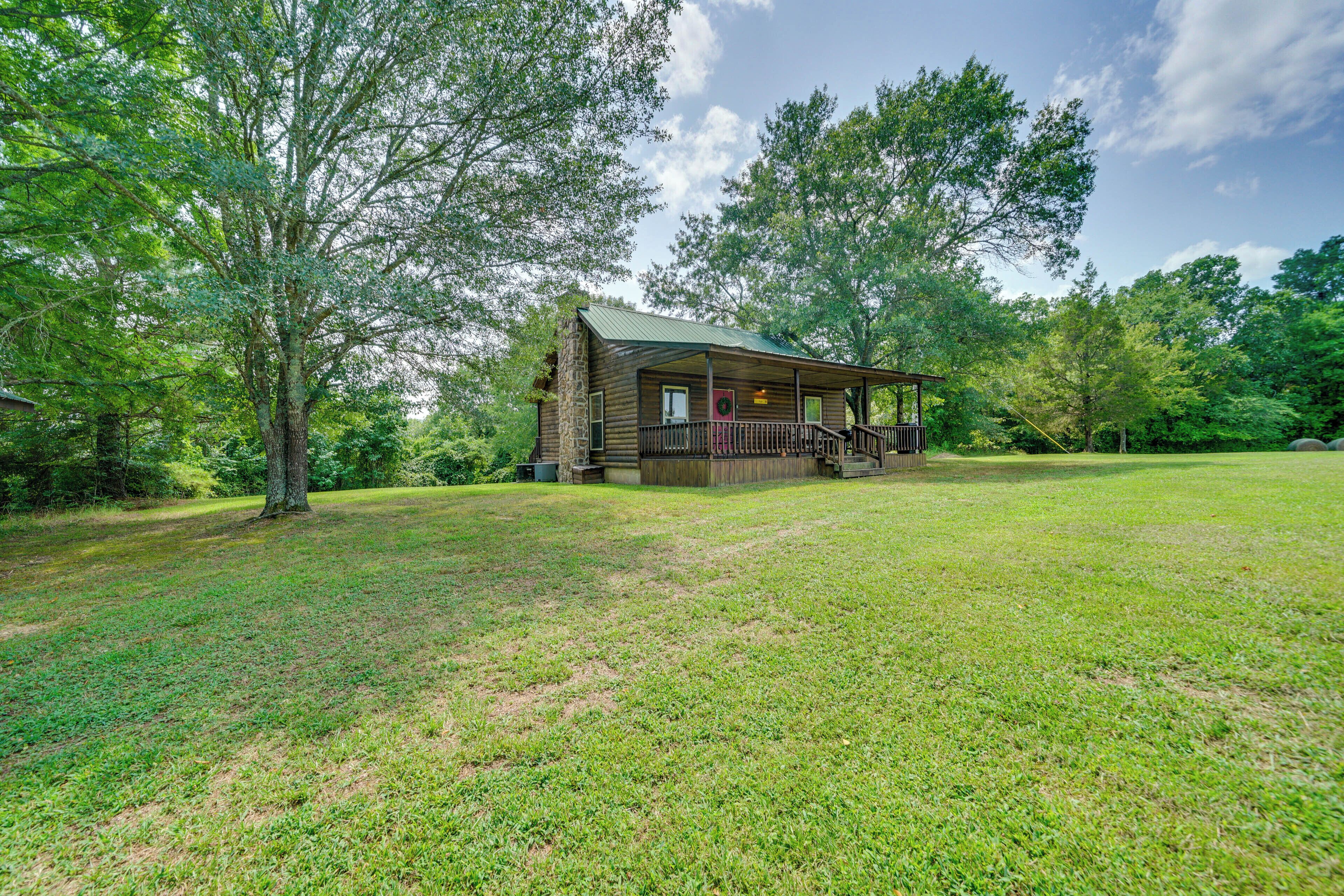 A rustic cabin with a porch, surrounded by a grassy field and trees.