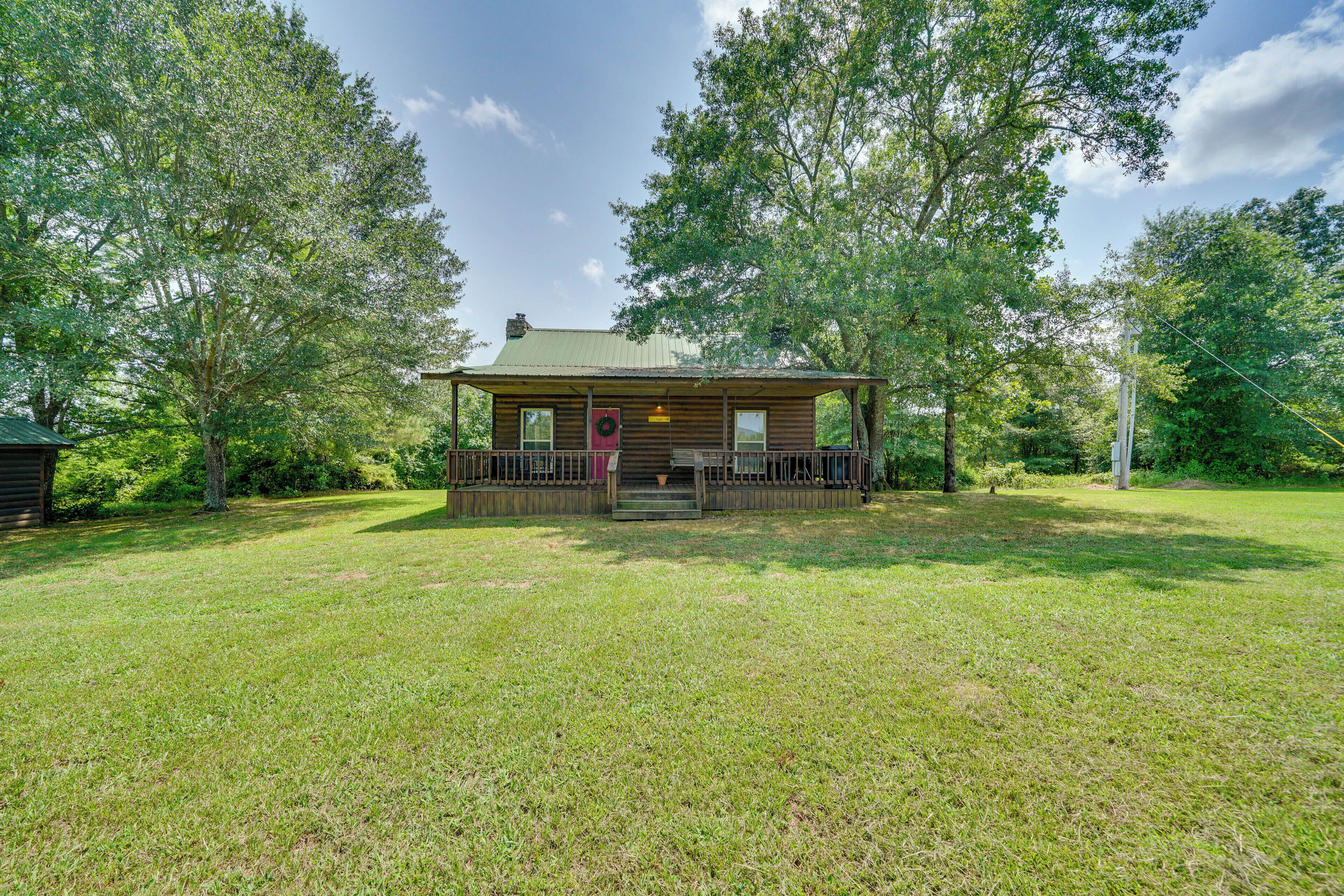 A wooden cabin with a porch, surrounded by a grassy yard and trees.