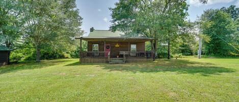 A wooden cabin with a porch, surrounded by a grassy yard and trees.