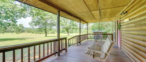 Un porche cubierto con una terraza de madera, una mecedora y vistas a un campo con árboles.