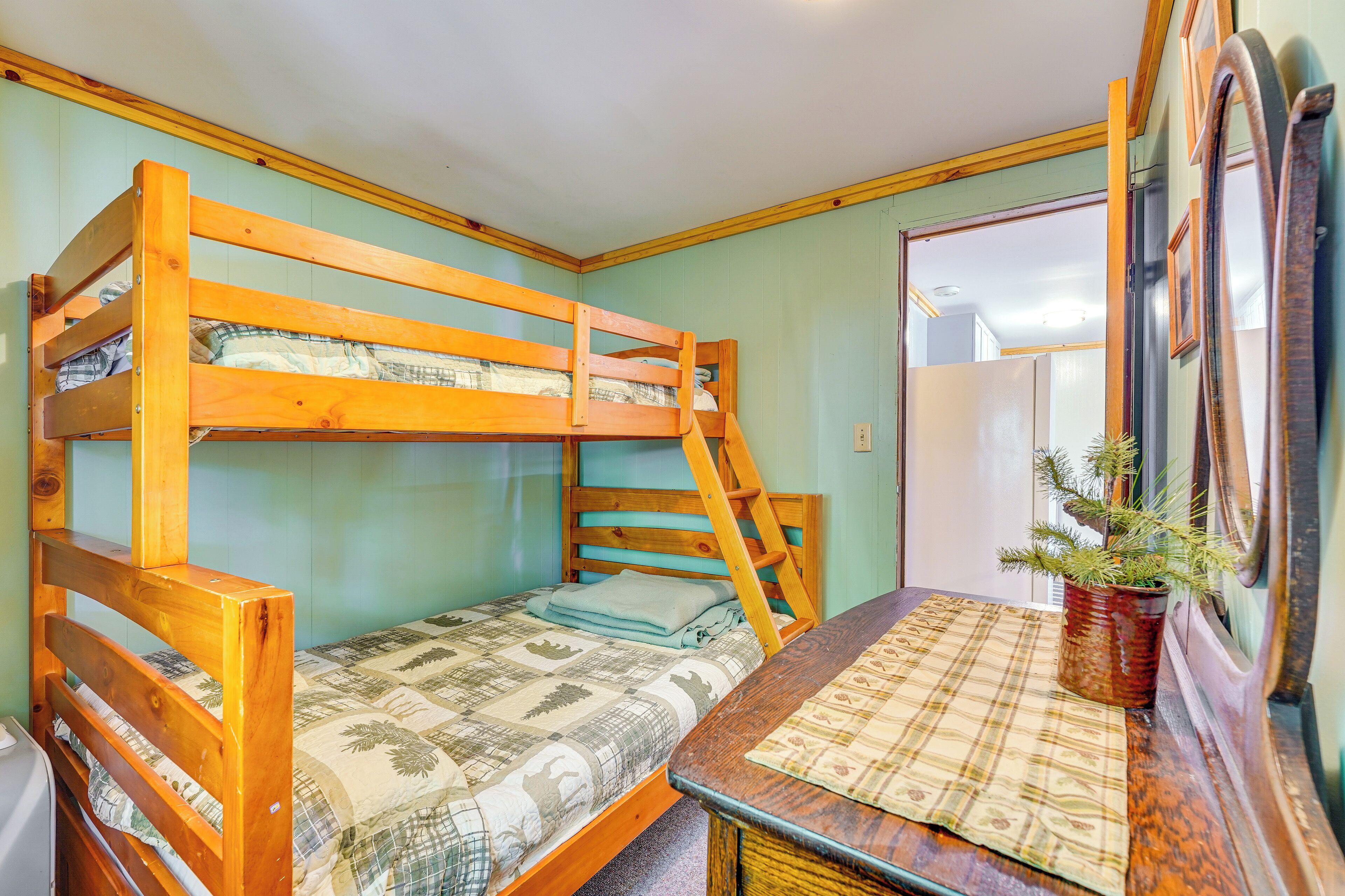 A bunk bed with a wooden frame and a quilted bedspread. There is a small table with a plaid tablecloth and a potted plant.