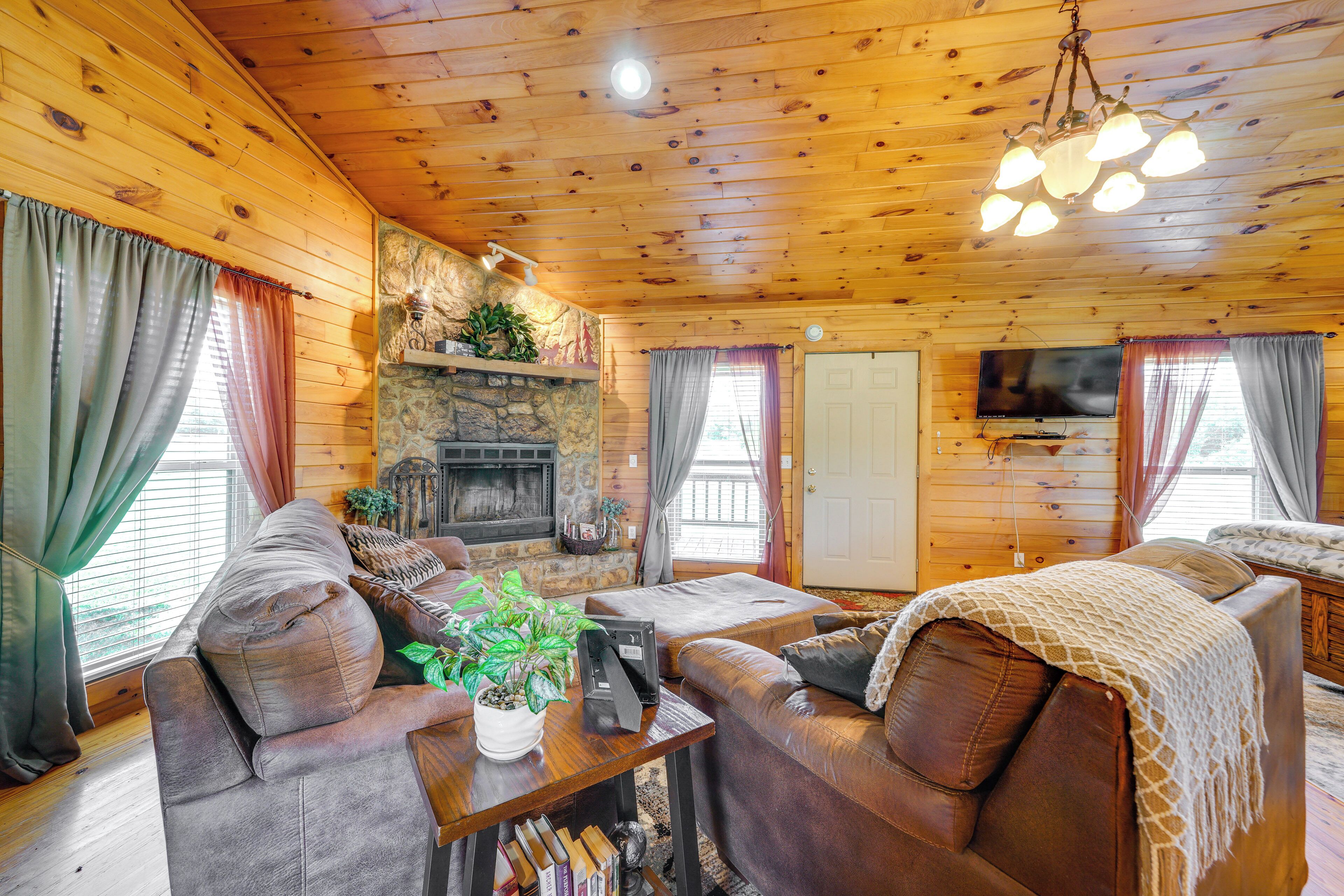 A cozy cabin interior with a stone fireplace, leather sofas, a television, and wooden walls.