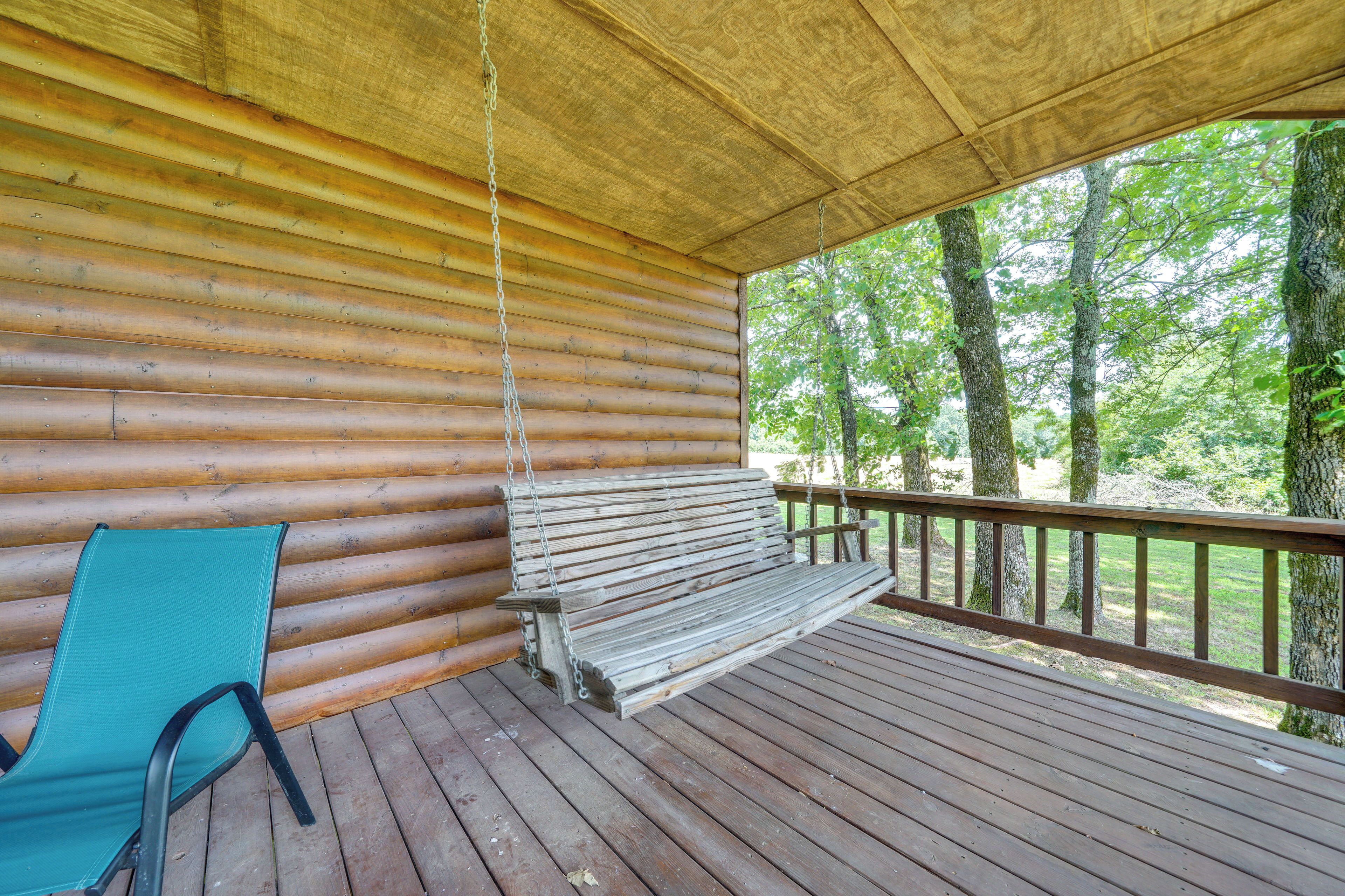 A wooden deck with a bench and a chair, overlooking a forested area.