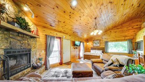 Ein gemütliches Blockhaus-Interieur mit Kamin aus Stein, Holzbalkendecke und einer komfortablen Sitzecke mit Sofa und Hocker.