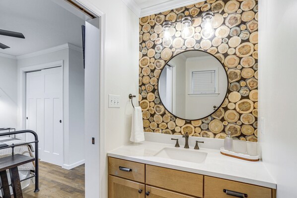 A bathroom with a wooden log wall, a round mirror, a white sink, and a wooden cabinet. - Treasure Lake Home w/ Deck: Walk to Bimini Lake! (DuBois)